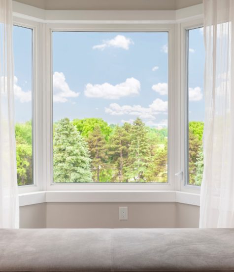 Bay window with drapes, curtains and view of trees under summer sky